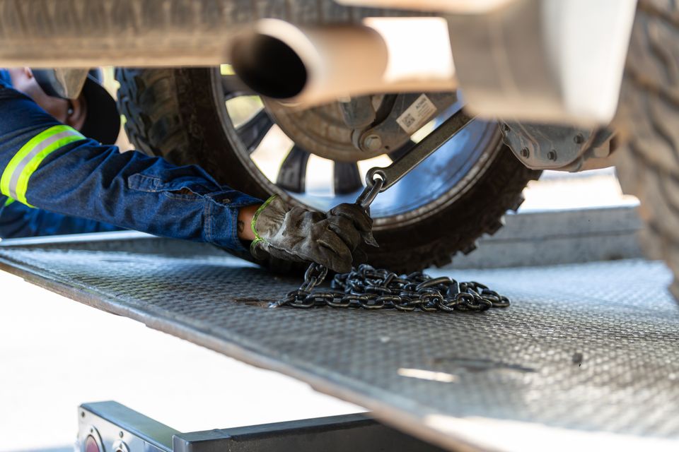 An operator in a hi vis jacket hooking a chain onto a vehicle on a flatbed deck
