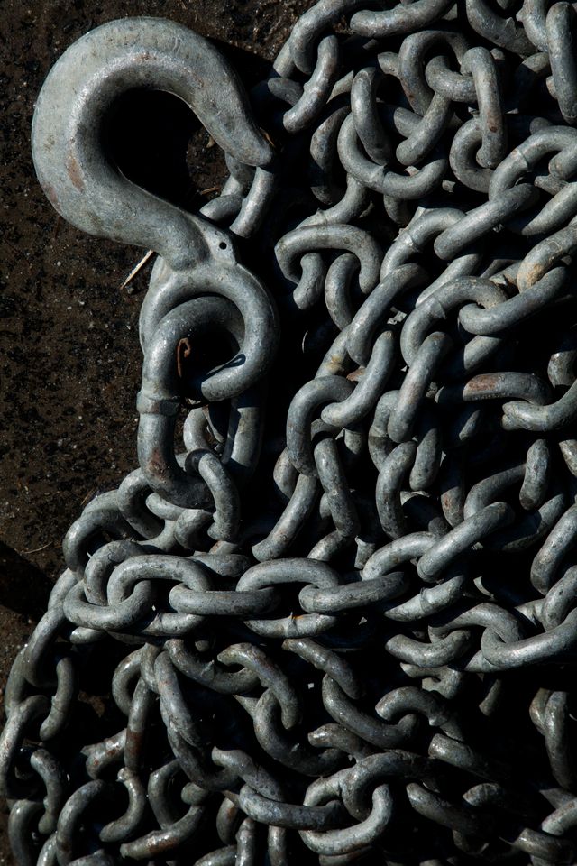 A galvanised tow hook lying on a coil of heavy chain on wet ground
